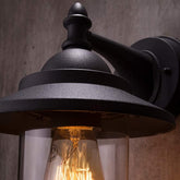 Black outdoor wall light fixture with a visible light bulb against a neutral background